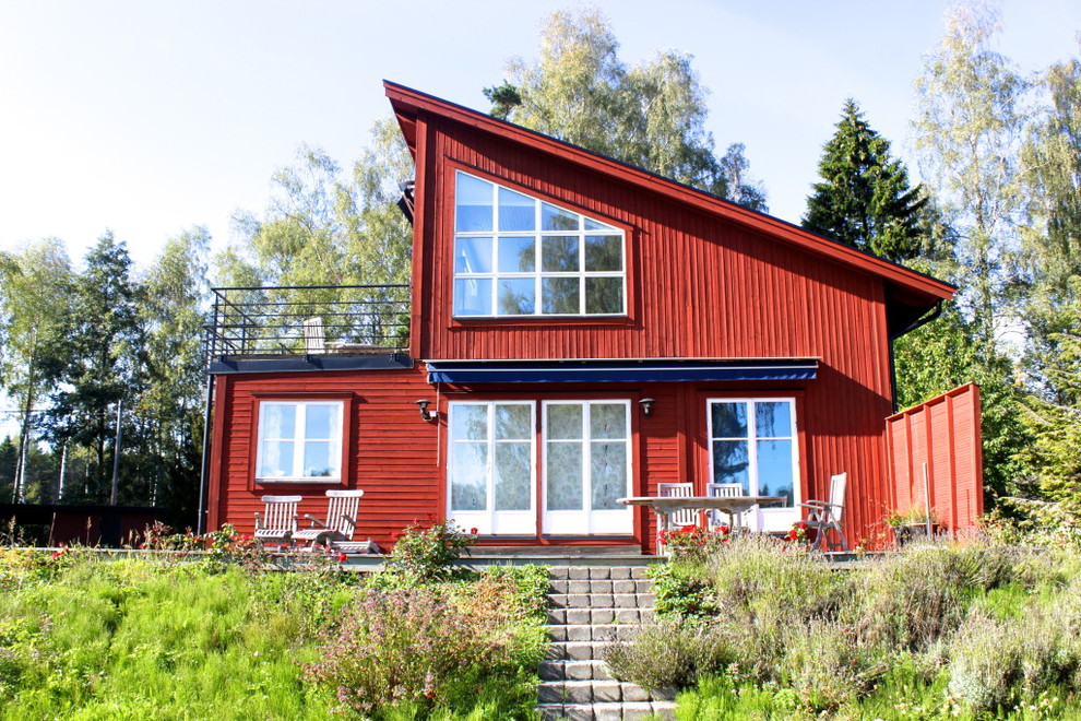 Bild på ett mellanstort skandinaviskt rött trähus, med två våningar och pulpettak