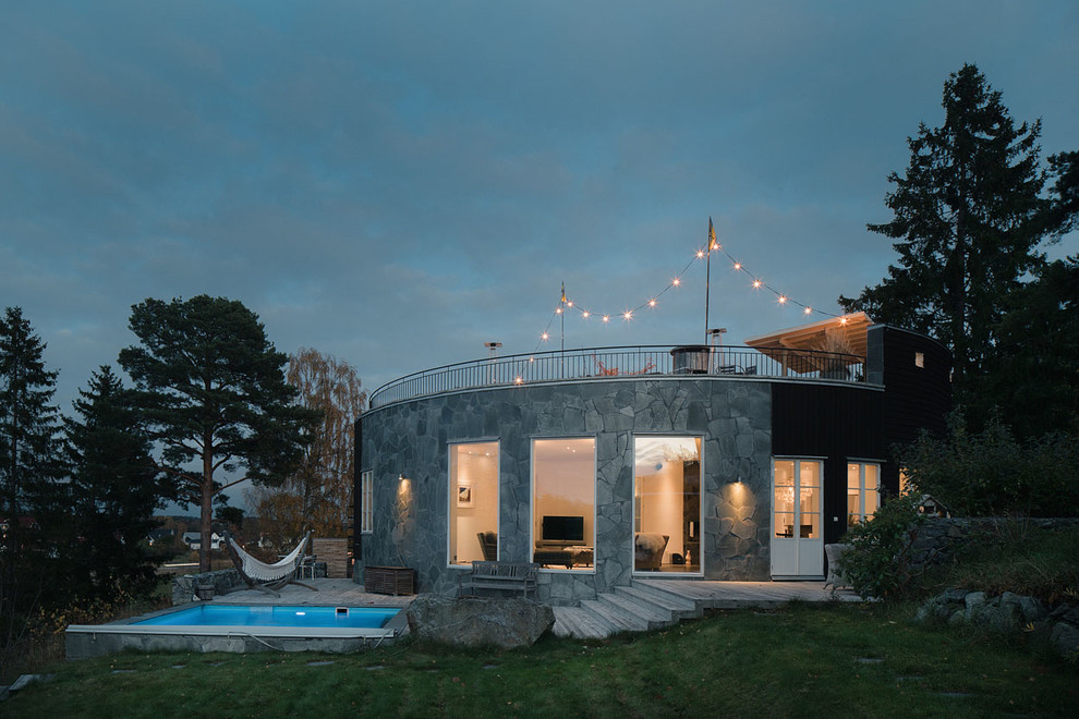 На фото: одноэтажный, серый частный загородный дом среднего размера в скандинавском стиле с облицовкой из камня и плоской крышей