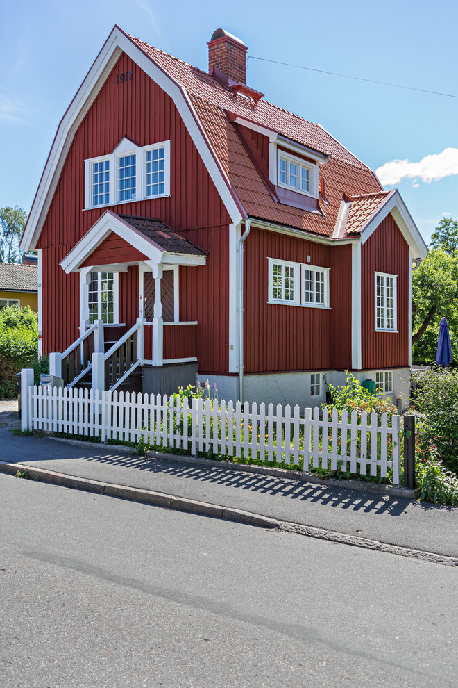 Large farmhouse red three-story wood house exterior idea in Stockholm with a gambrel roof and a tile roof