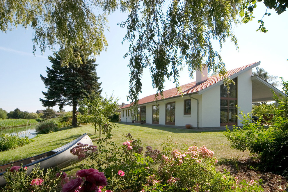 Diseño de fachada de casa blanca nórdica de una planta con revestimiento de estuco, tejado de un solo tendido y tejado de teja de barro