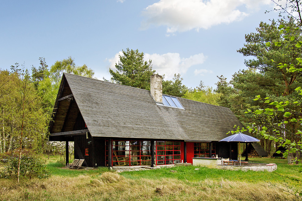 Cette photo montre une grande façade de maison noire scandinave en verre à un étage avec un toit à deux pans.
