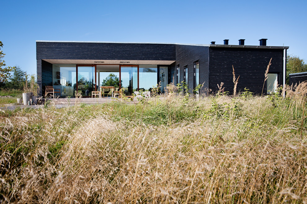 This is an example of a small and black contemporary house exterior in Aalborg with wood cladding and a flat roof.