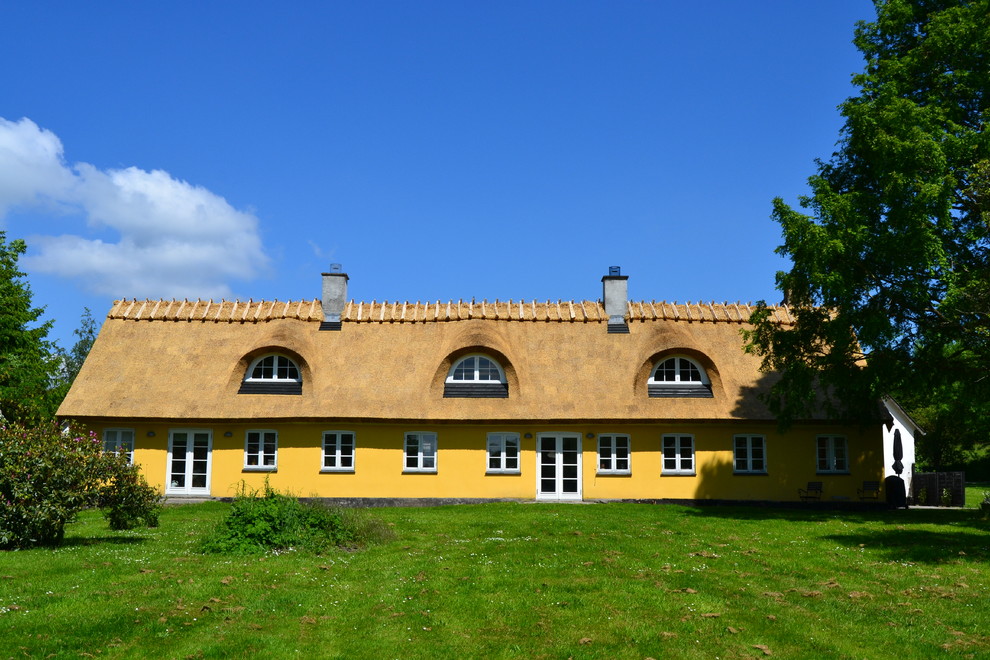 Modelo de fachada amarilla de estilo de casa de campo grande de dos plantas con revestimiento de ladrillo y tejado a la holandesa