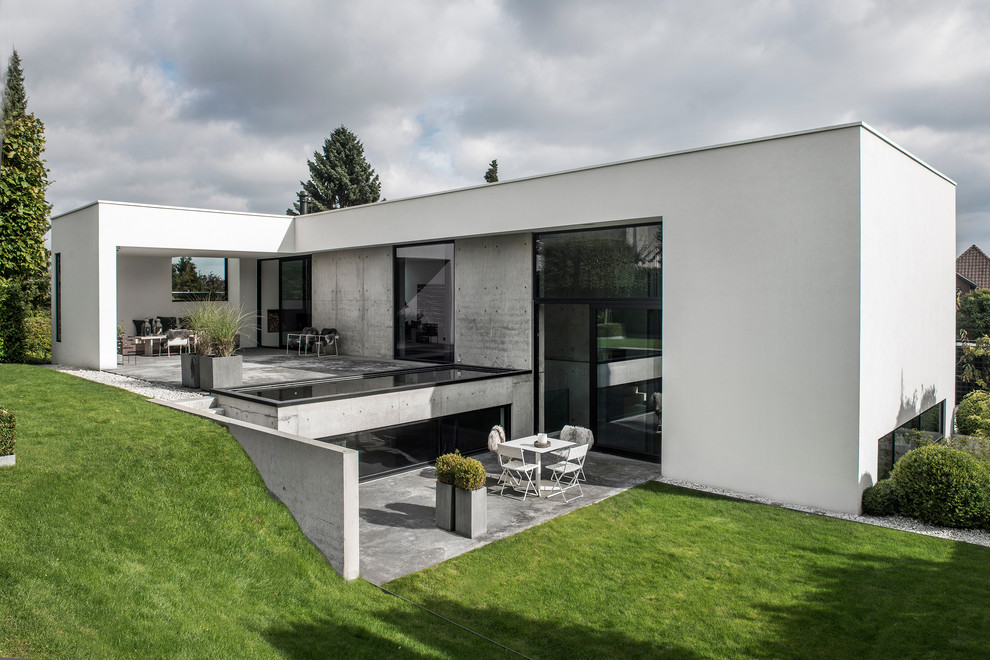 Cette image montre une grande façade de maison blanche minimaliste en brique à niveaux décalés avec un toit plat.