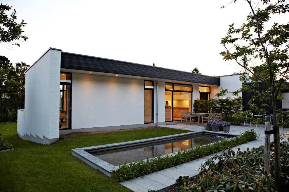 На фото: белый частный загородный дом в стиле модернизм с разными уровнями, облицовкой из крашеного кирпича, плоской крышей и черной крышей