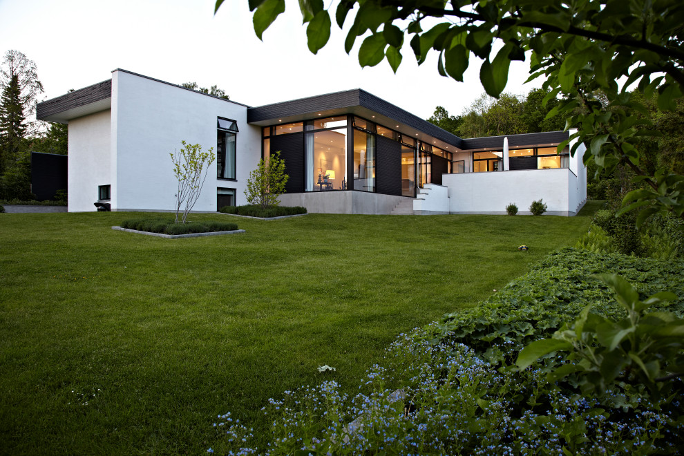 Пример оригинального дизайна: белый частный загородный дом в стиле модернизм с разными уровнями, облицовкой из крашеного кирпича, плоской крышей и черной крышей