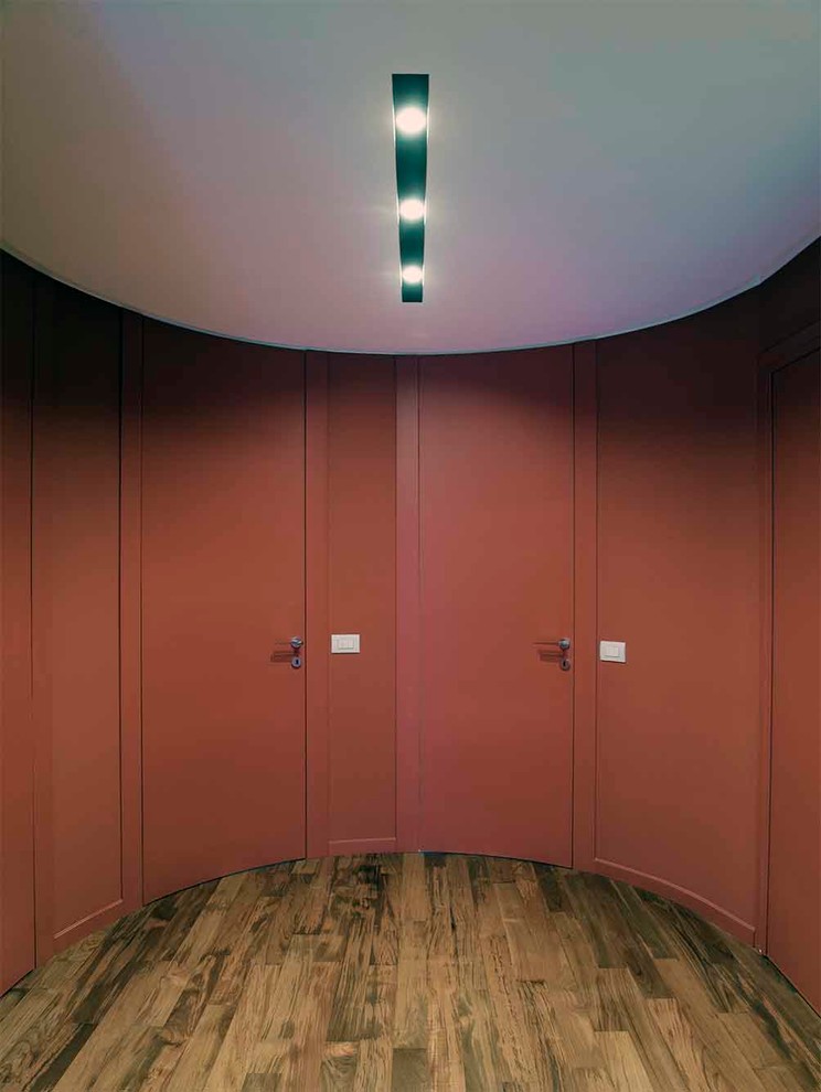 This is an example of a medium sized contemporary foyer in Milan with red walls, medium hardwood flooring, a single front door and a red front door.