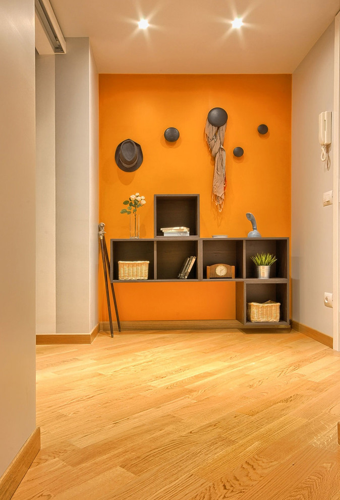 Ejemplo de distribuidor minimalista de tamaño medio con parades naranjas, suelo de madera clara, puerta doble y puerta blanca
