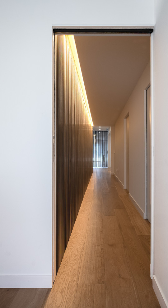Cette image montre un couloir design de taille moyenne avec un mur blanc, parquet clair et un sol beige.