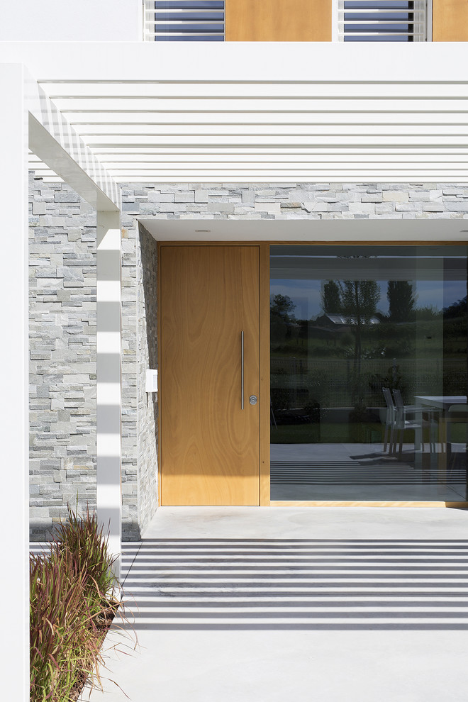 Réalisation d'une entrée design avec sol en béton ciré et une porte en bois clair.