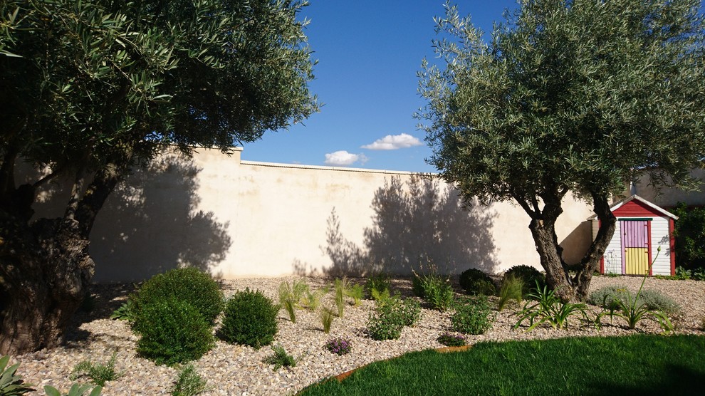 Modelo de jardín mediterráneo de tamaño medio en patio trasero con exposición parcial al sol y gravilla
