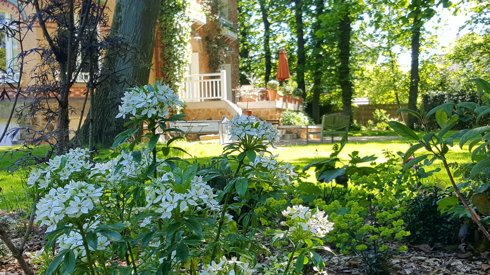 Großer, Schattiger Shabby-Look Garten im Frühling, hinter dem Haus mit Blumenbeet und Mulch in Sonstige