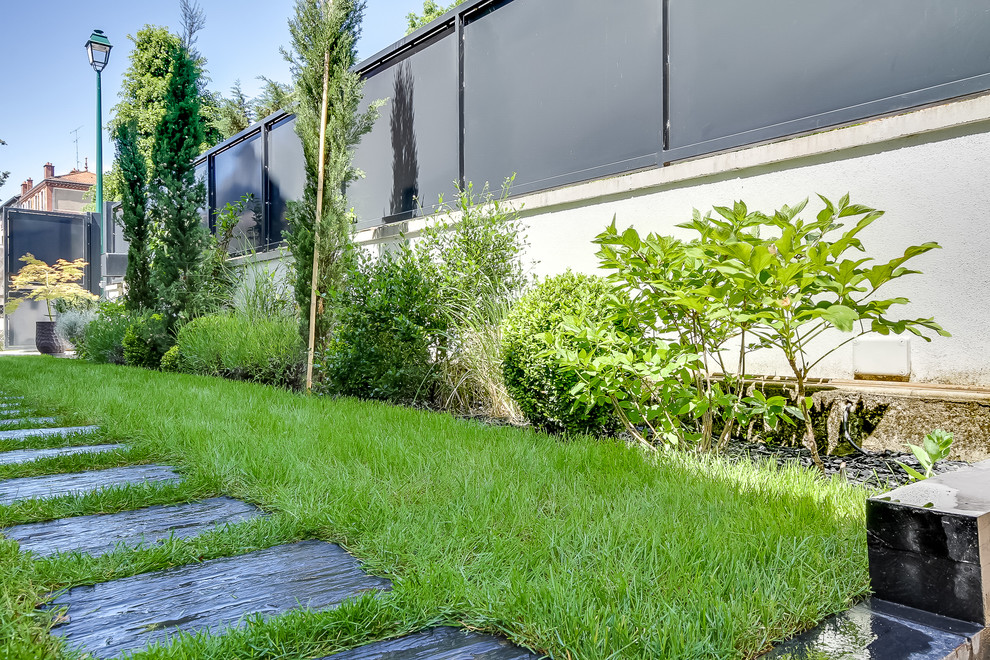 Exemple d'un jardin arrière moderne de taille moyenne et l'été avec une exposition partiellement ombragée, des pavés en pierre naturelle et une clôture en pierre.