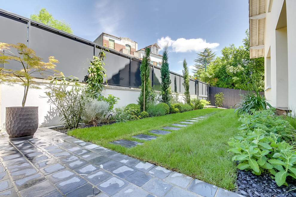Cette image montre un jardin arrière minimaliste de taille moyenne et l'été avec une exposition partiellement ombragée, des pavés en pierre naturelle et une clôture en pierre.