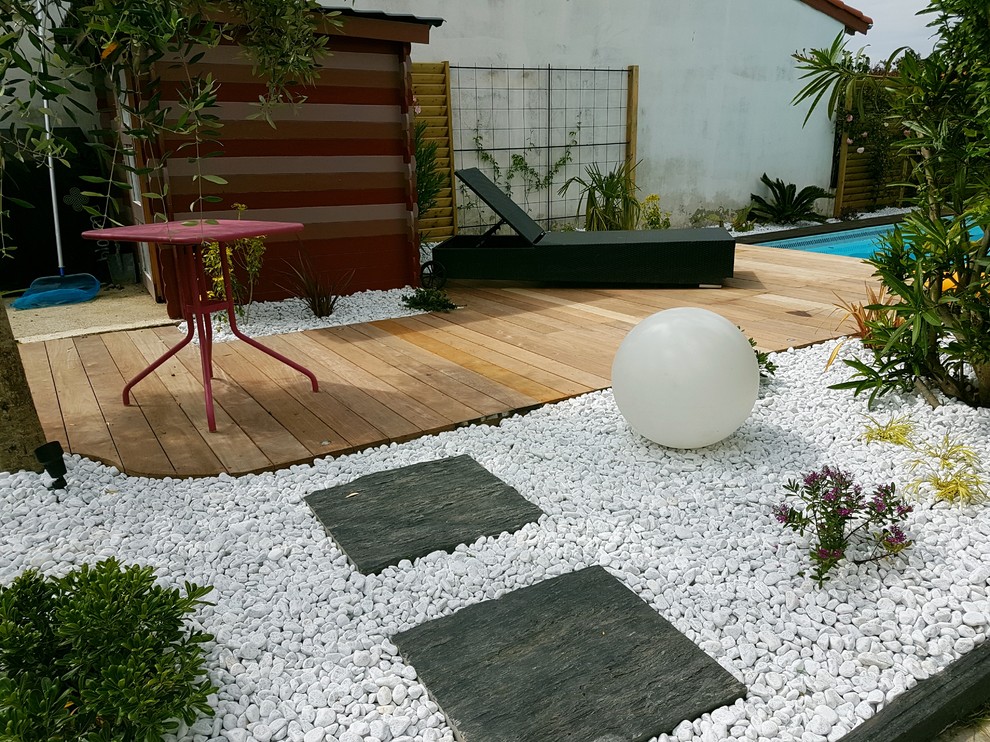 Réalisation d'un petit jardin latéral design l'été avec un mur de soutènement, une exposition ombragée et une terrasse en bois.