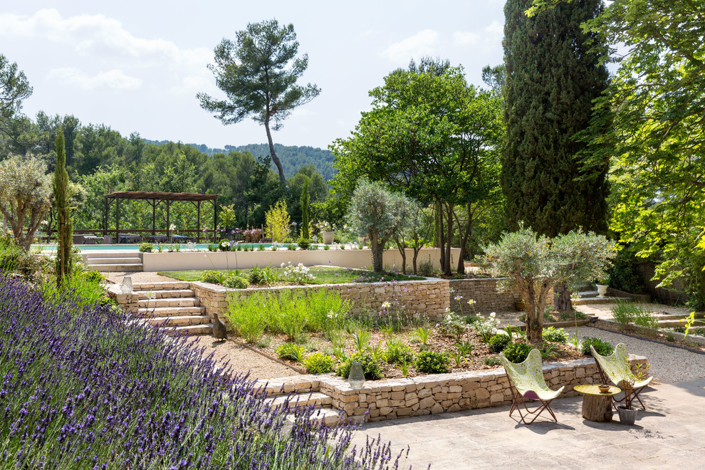 На фото: регулярный сад на заднем дворе в средиземноморском стиле с подпорной стенкой и покрытием из каменной брусчатки с