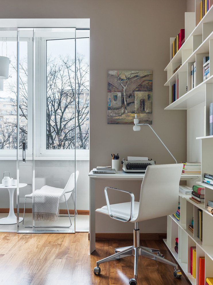 Contemporary study in Moscow with medium hardwood flooring, a built-in desk, brown floors and grey walls.