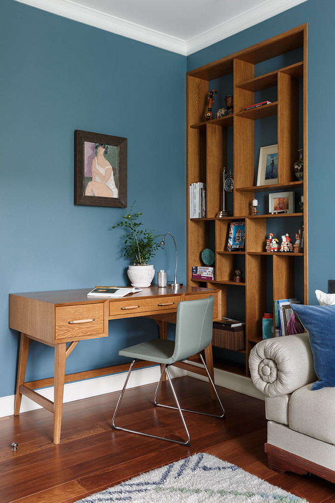 Foto på ett funkis hemmabibliotek, med blå väggar, mellanmörkt trägolv, ett fristående skrivbord och brunt golv