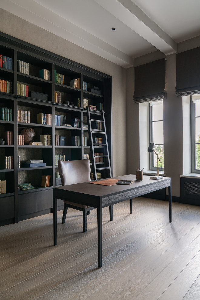 Classic study in Moscow with beige walls, light hardwood flooring, a freestanding desk and beige floors.