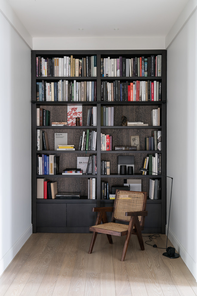 Ejemplo de despacho actual con biblioteca, paredes blancas, suelo de madera clara y suelo beige