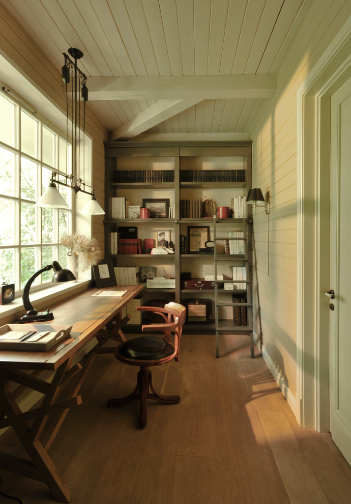 Modern inredning av ett litet arbetsrum, med ett bibliotek, beige väggar, ljust trägolv, ett fristående skrivbord och beiget golv