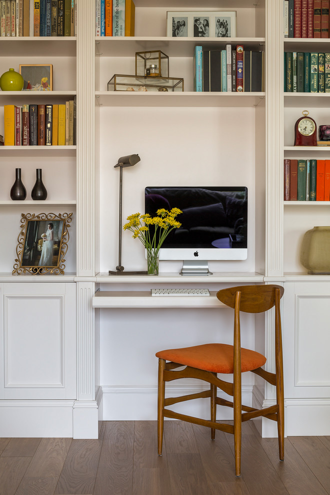 Modelo de despacho tradicional renovado pequeño con paredes blancas, suelo de madera en tonos medios y escritorio empotrado