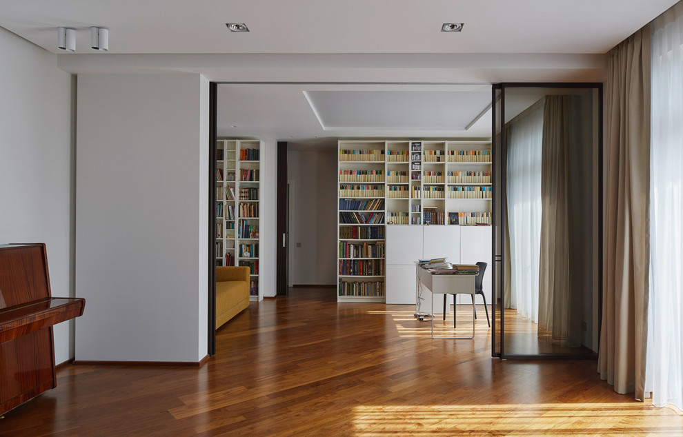 Idéer för ett modernt hemmabibliotek, med vita väggar, mellanmörkt trägolv och ett fristående skrivbord