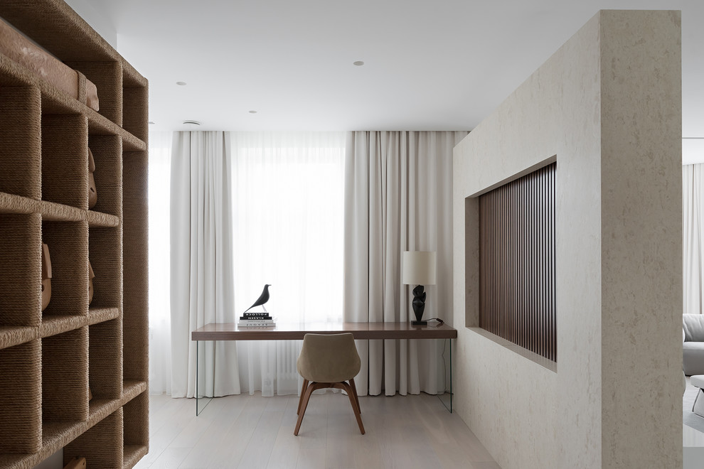 Diseño de despacho actual con paredes beige, suelo de madera clara, escritorio independiente y suelo beige