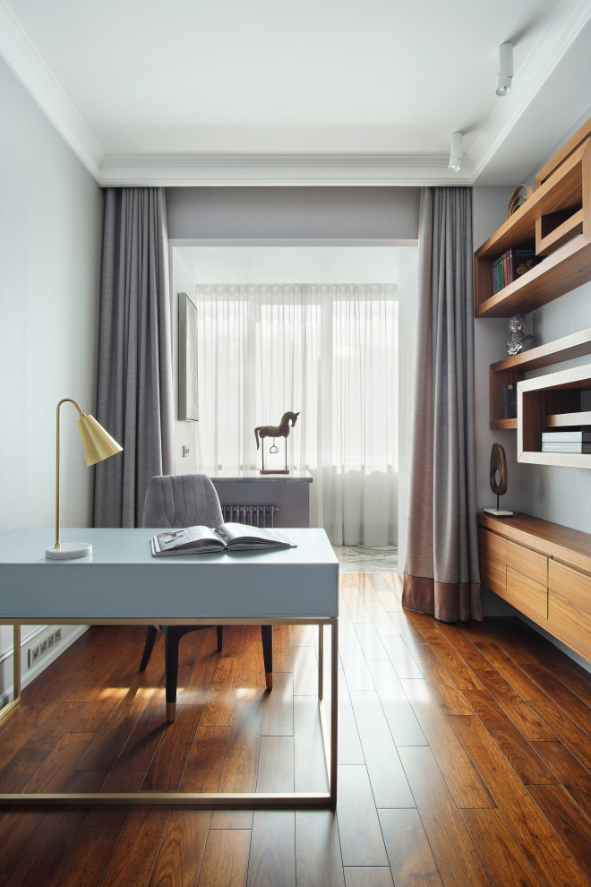 Mittelgroßes Modernes Arbeitszimmer mit Arbeitsplatz, grauer Wandfarbe, braunem Holzboden, freistehendem Schreibtisch und braunem Boden in Sonstige