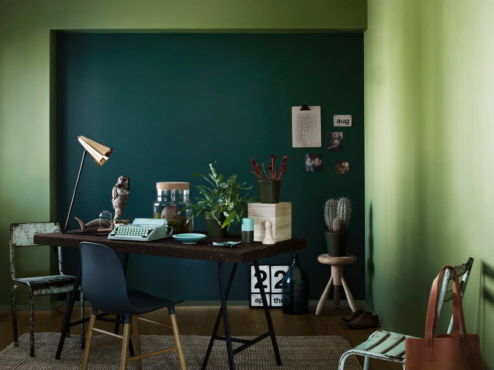 Inredning av ett modernt hemmabibliotek, med gröna väggar, mellanmörkt trägolv, ett fristående skrivbord och brunt golv