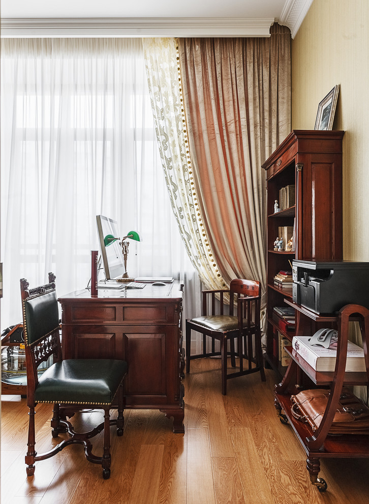 Modelo de despacho tradicional grande sin chimenea con escritorio independiente, paredes beige y suelo de madera en tonos medios