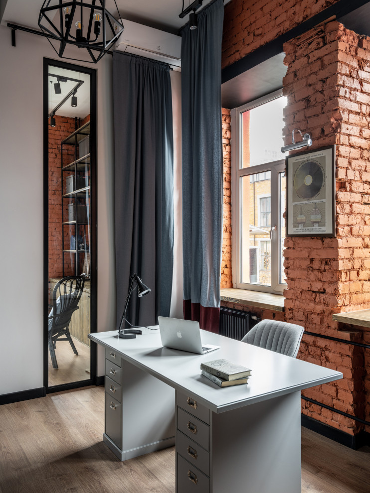 Стильный дизайн: кабинет в стиле лофт с серыми стенами, паркетным полом среднего тона, отдельно стоящим рабочим столом, коричневым полом и кирпичными стенами - последний тренд