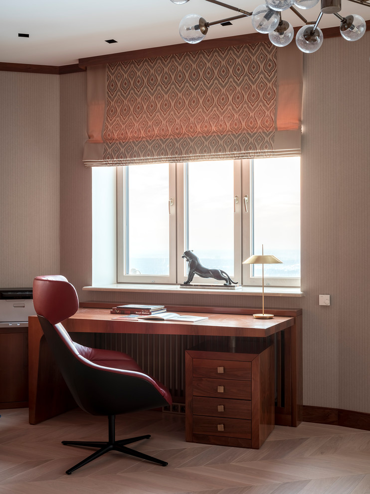 Ejemplo de despacho actual con paredes beige, suelo de madera clara, escritorio independiente y suelo beige