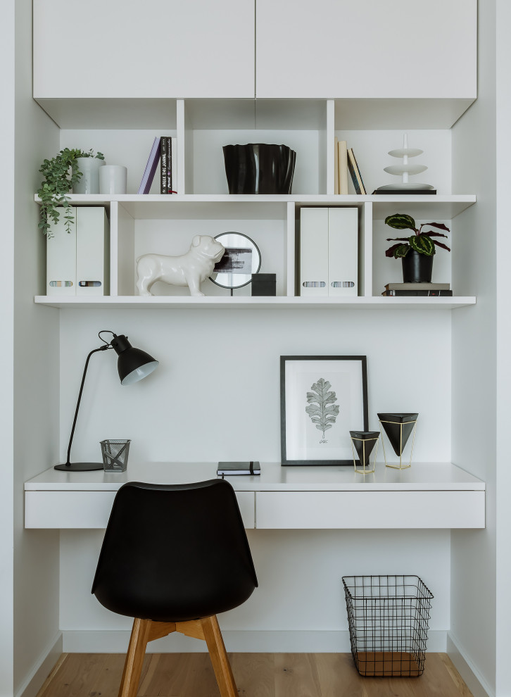Diseño de despacho actual con paredes blancas, escritorio empotrado, suelo de madera clara y suelo beige