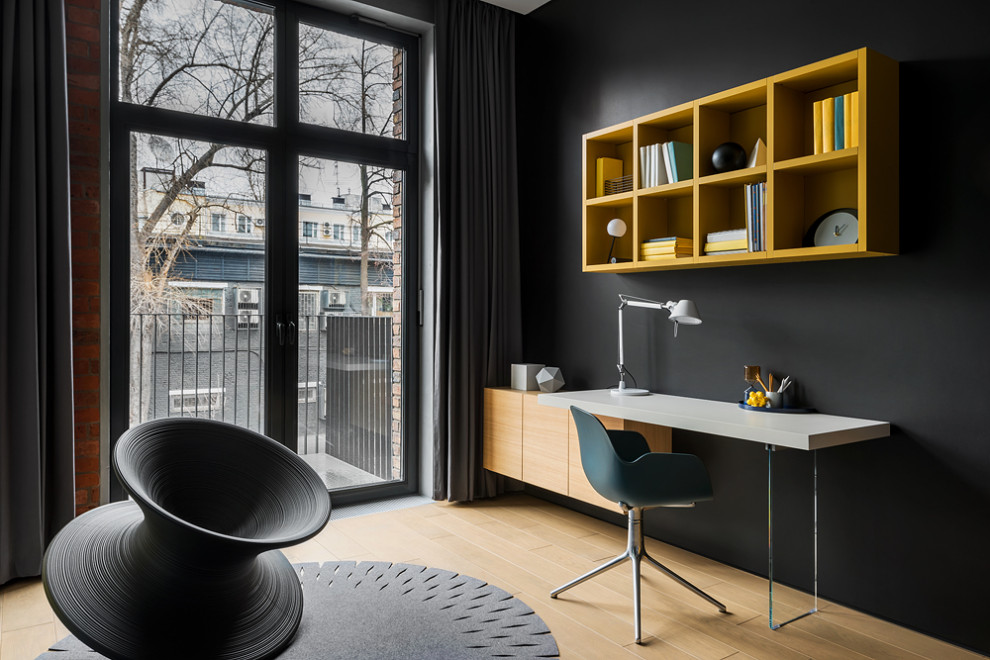 This is an example of a medium sized modern study in Moscow with black walls, light hardwood flooring, a built-in desk, beige floors and brick walls.