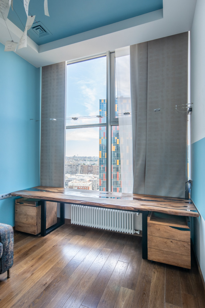 Imagen de despacho actual grande sin chimenea con paredes azules, suelo laminado, escritorio independiente y suelo marrón