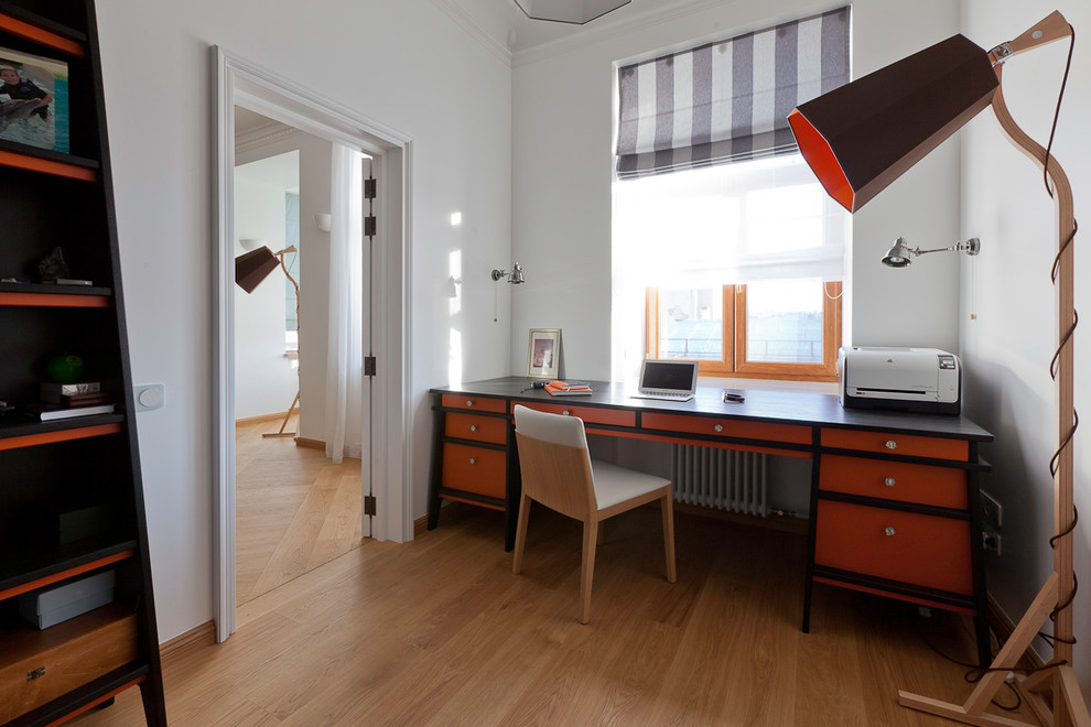 Imagen de despacho actual pequeño con biblioteca, paredes blancas, suelo de madera clara, escritorio independiente y suelo marrón
