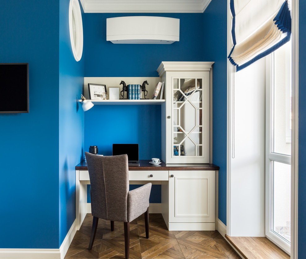 Пример оригинального дизайна: рабочее место среднего размера в стиле неоклассика (современная классика) с синими стенами, деревянным полом, отдельно стоящим рабочим столом, коричневым полом и многоуровневым потолком