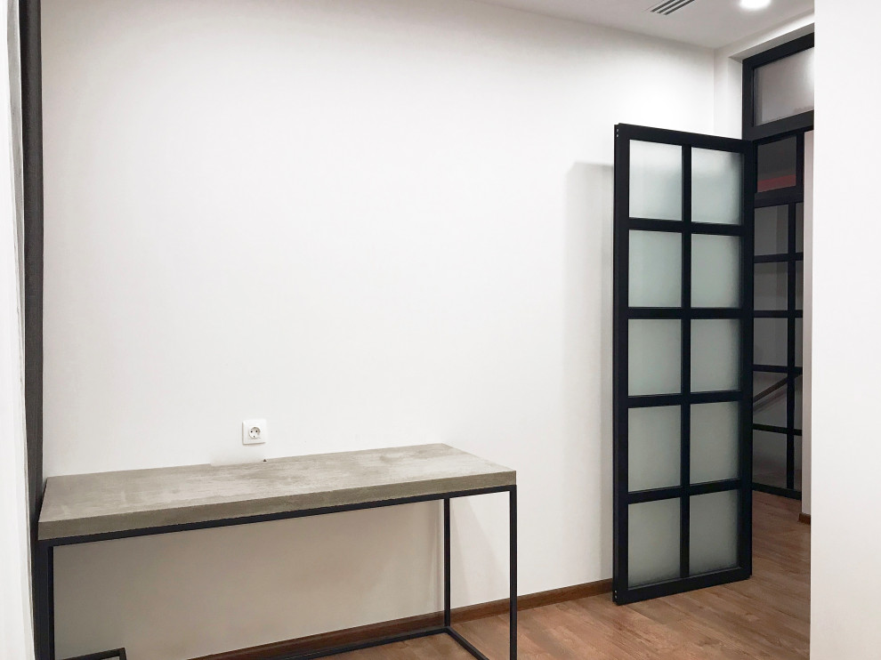 Diseño de despacho actual de tamaño medio con paredes blancas, suelo laminado, escritorio independiente y bandeja