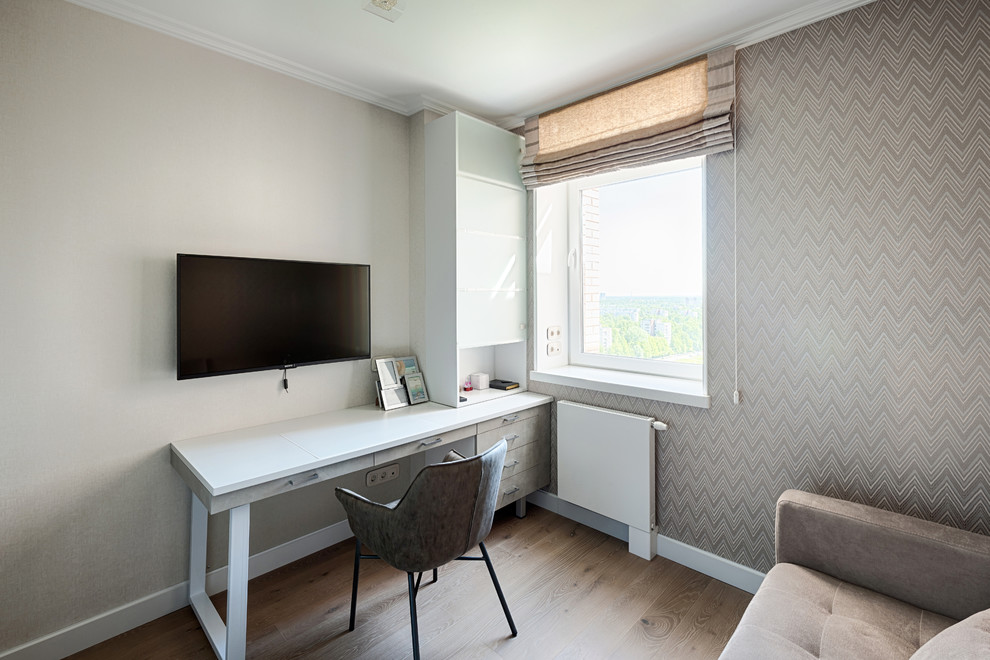 Modelo de despacho contemporáneo de tamaño medio con paredes beige, suelo laminado, escritorio independiente y suelo marrón