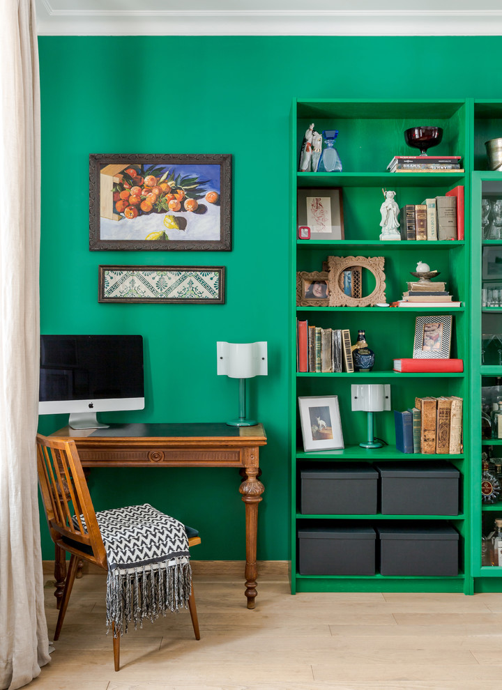 Foto på ett eklektiskt hemmabibliotek, med gröna väggar, ljust trägolv, ett fristående skrivbord och beiget golv