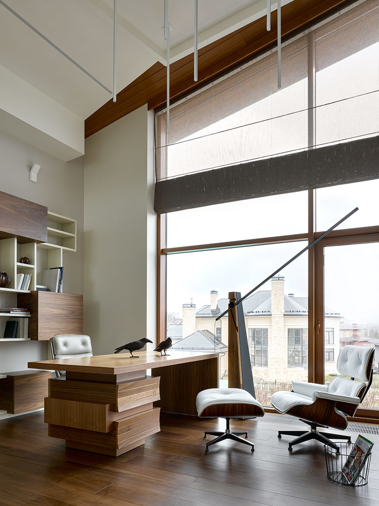 Пример оригинального дизайна: рабочее место в современном стиле с белыми стенами, темным паркетным полом, отдельно стоящим рабочим столом и коричневым полом