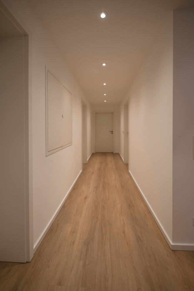 This is an example of a medium sized modern fully buried basement in Munich with beige walls, vinyl flooring and brown floors.