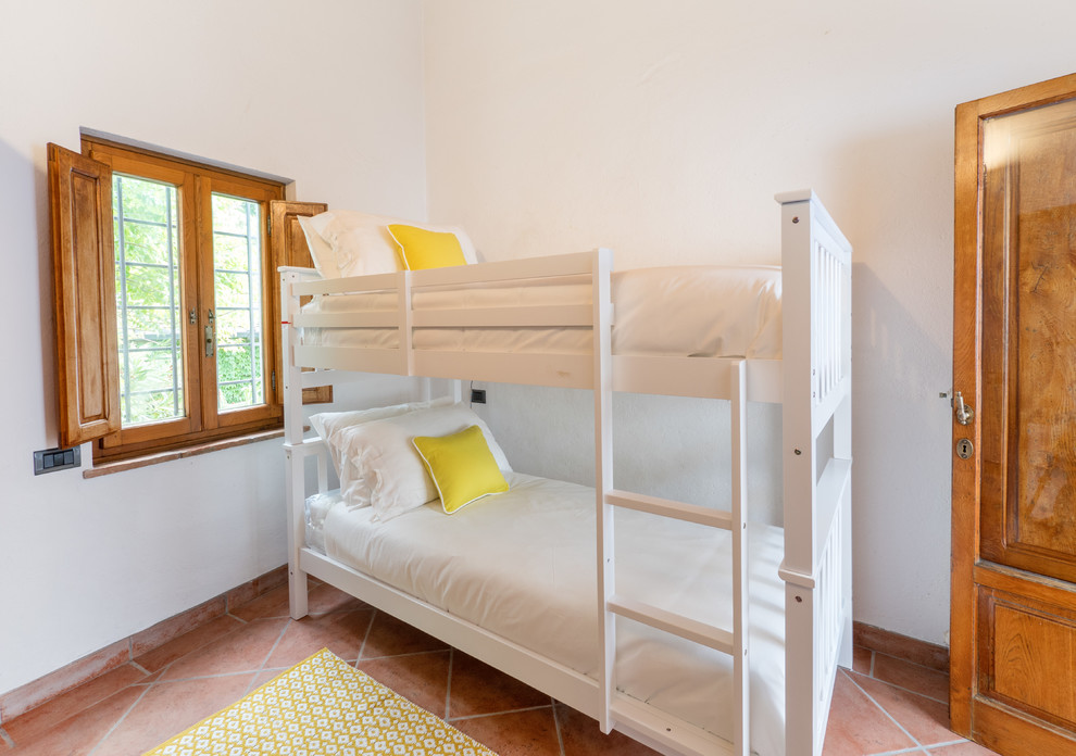 Cette image montre une petite chambre d'enfant rustique avec un mur blanc, tomettes au sol, un sol orange et un lit superposé.