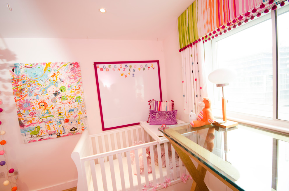 Photo of a small classic toddler’s room for girls in London with pink walls, light hardwood flooring and brown floors.