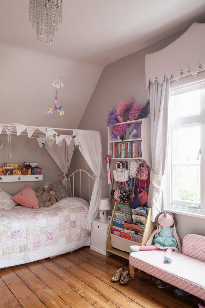 This is an example of a medium sized bohemian children’s room for girls in West Midlands with pink walls, medium hardwood flooring and brown floors.