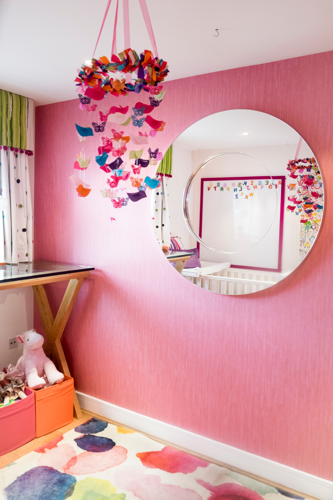 Esempio di una piccola cameretta per bambini da 1 a 3 anni moderna con pareti rosa e pavimento in legno massello medio