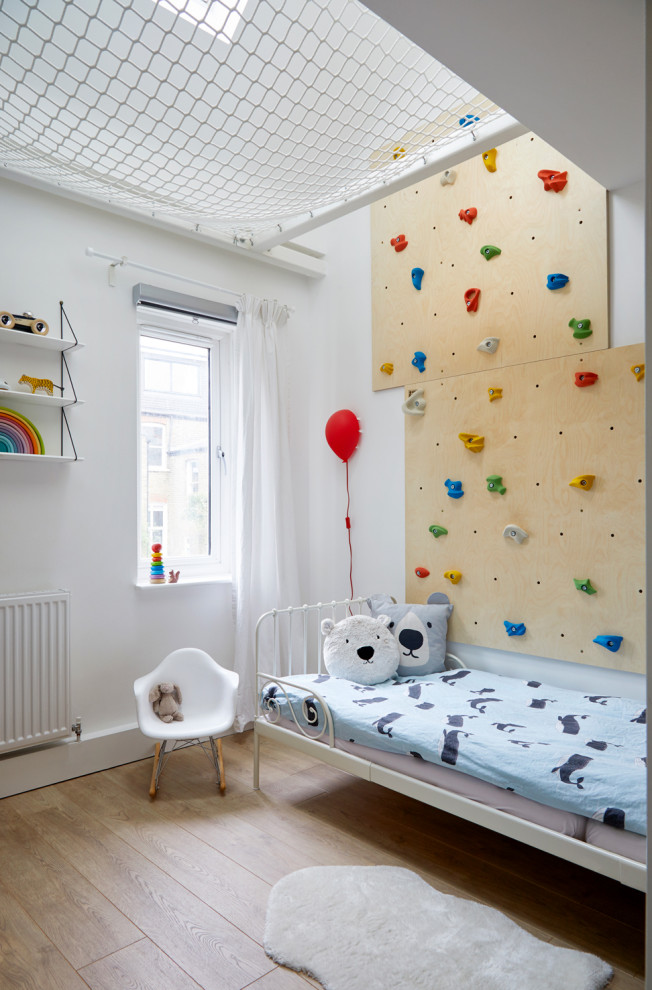 Example of a trendy gender-neutral medium tone wood floor and brown floor kids' bedroom design in London with white walls