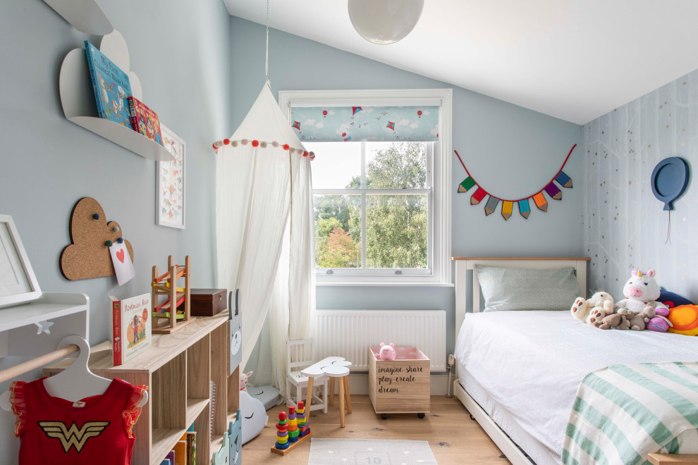 Photo of a contemporary toddler’s room for girls in London with blue walls, medium hardwood flooring and brown floors.