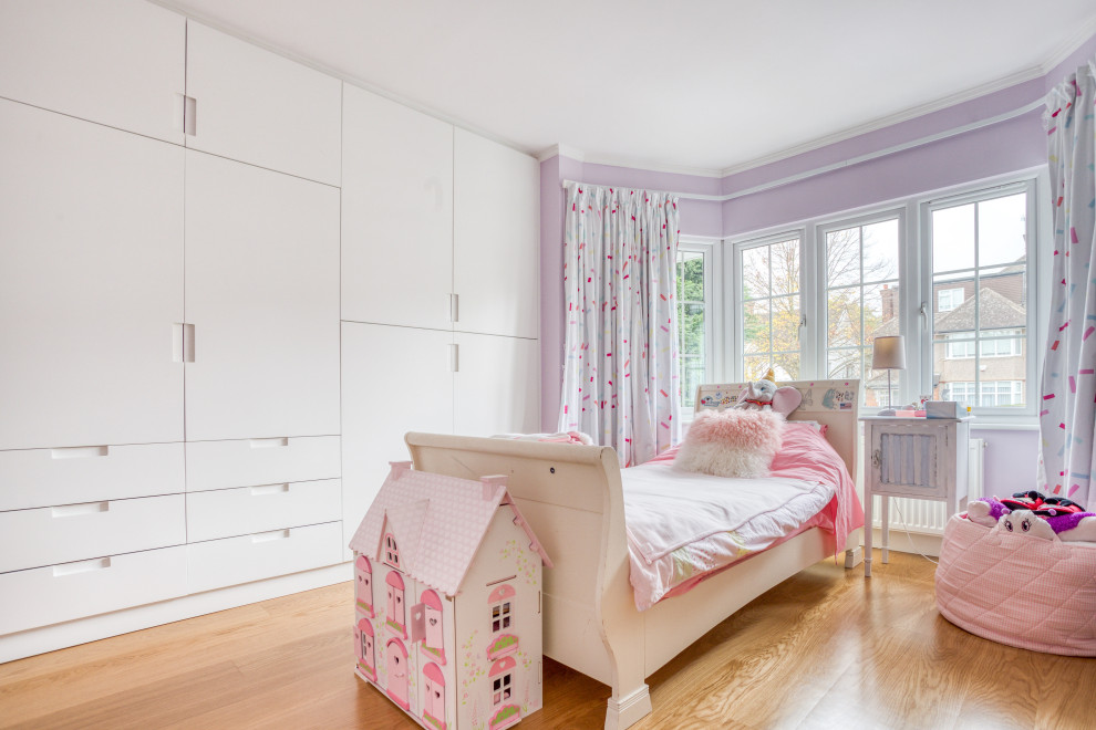 Medium sized contemporary children’s room for girls in London with purple walls, medium hardwood flooring and beige floors.